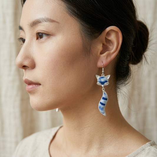 Side profile view of a woman wearing a single handcrafted indigo dye fox dangle earring, showing its scale and whimsical design against her face.